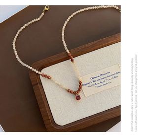 Detail of beaded natural stone necklace with vintage red gemstone pendant on tray