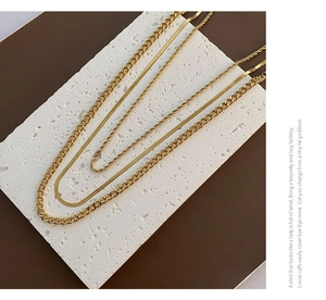 Detailed view of layered 18K gold-plated snake and Cuban chain necklaces on marble