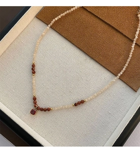 Detailed close-up of a natural stone beaded necklace with a square red gem pendant on fabric