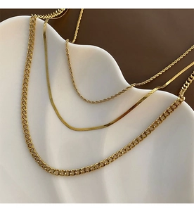 Close-up of triple-layered gold necklaces with curb, snake and rope chains on a white tray
