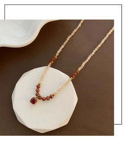 Detail of beaded necklace featuring gold-rimmed red gemstone and sparkling goldstone beads
