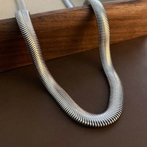 Polished silver stainless steel flat snake chain necklace on a leather stand