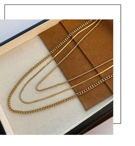 Detailed view of layered 18K gold stainless steel snake, curb, and rope chains on a tray