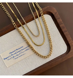 Detailed close-up of layered gold Cuban, snake and rope chain necklaces on a jewelry tray