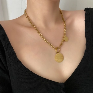 Gold titanium chain necklace with OT buckle and circular engraved pendants on a black top