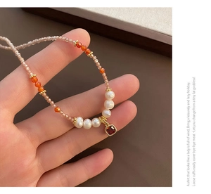 Nahaufnahme einer Perlenkette mit rotem quadratischem Edelsteinanhänger und Orangenperlen