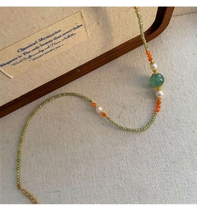 Detail of beaded necklace with light green zircon, pearls, and gold clasp on linen texture