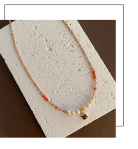 Detailaufnahme der Zirkon-Perlenkette mit rotem Edelstein-Anhänger auf weißem Stein