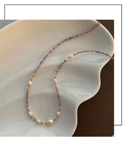 Close-up of purple beads and pearl necklace with golden lobster clasp on shell plate