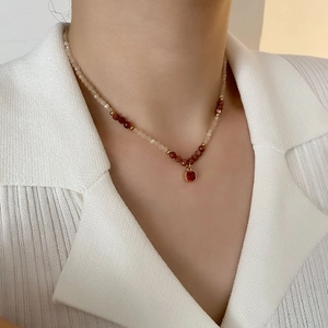 Vintage beaded necklace with deep red gemstone pendant on a white striped shirt