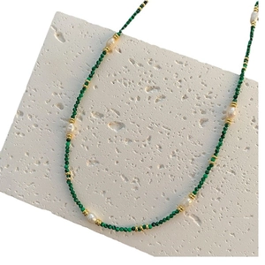 Malachite and freshwater pearl necklace with gold accents on a white stone background