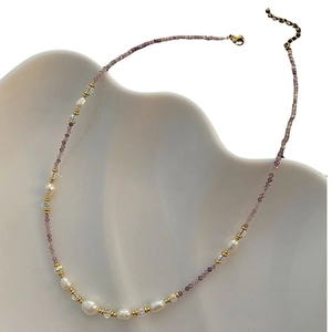 Elegant purple stone and pearl beaded necklace with gold accents on white ceramic plate