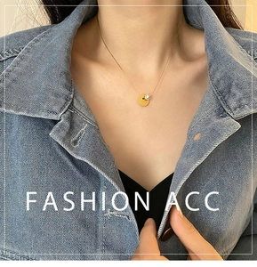 Close-up of gold coin pendant with pearl on a stainless steel necklace worn by a model