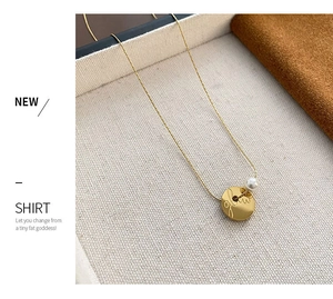 Detail of gold coin necklace with glow engraving and white pearl on textured tray