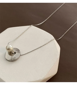 Detail of silver chain necklace with pearl and engraved coin on geometric stone base