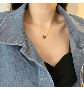 Close-up of gold coin pendant and white pearl necklace worn on a blue denim jacket