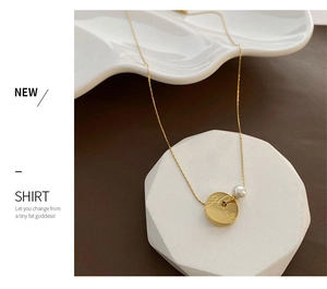 Detailed close-up of a gold coin pendant with white pearl on a delicate fine chain necklace
