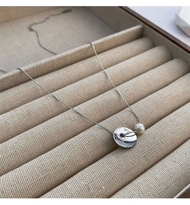 Detailed macro view of a titanium steel coin pendant with a white pearl and silver chain