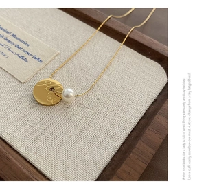Close-up of gold coin pendant necklace with white pearl on a rustic wooden tray