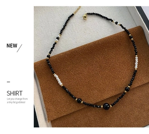 Detail of beaded necklace with black beads, white pearls, and gold-plated lobster clasp