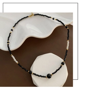 Detail of beaded choker necklace with black faceted beads, white pearls and gold accents