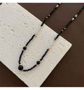 Detail of beaded necklace with black faceted beads and white pearls on white stone slab