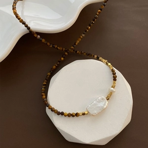 Collier en perles baroques et pierres œil de tigre sur un support d'art blanc