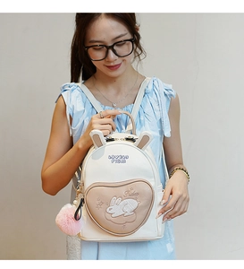 Close-up of white rabbit backpack featuring a heart-shaped pocket and pink fur ball charm