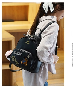 Detailed view of black mini backpack featuring cartoon bear patch and pink fur ball charm