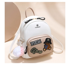 Close-up of mini backpack featuring embroidered cartoon bear and plush ball pendant