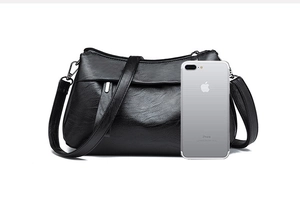 Detail of black pebbled leather crossbody bag with adjustable strap and phone for scale