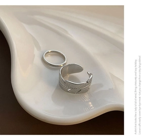 Detailed view of silver feather open ring and simple band set in a shell tray