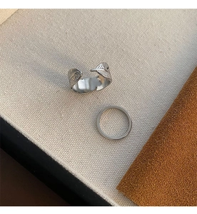 Detail of silver feather ring and minimalist thin band on textured fabric background