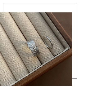 Macro detail of silver feather ring and sleek band set in a linen jewelry display tray