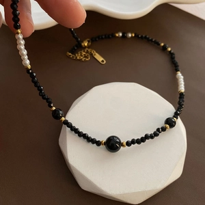 Elegant black beaded choker necklace with white pearls and gold accents on a display stand