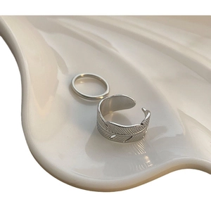 Minimalist silver feather ring set on white ceramic tray with polished vintage texture