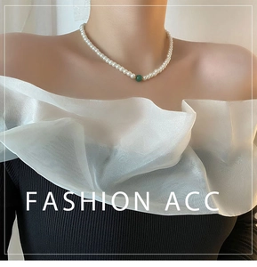 Detail of French glass pearl necklace featuring a single green bead on a female model