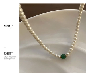 Close-up of pearl necklace with green bead on a textured white ceramic tray