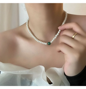 Close-up of pearl necklace with a green bead accent on a model wearing white blouse