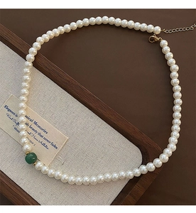 Detail of French glass pearl necklace with vintage green bead and gold clasp on tray