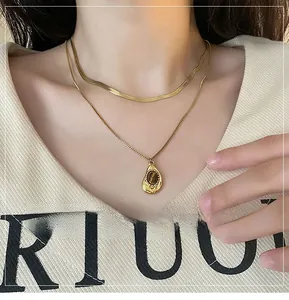 Close-up of gold layered necklace with flat snake chain and tiger eye water drop pendant