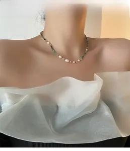 Detail of beaded necklace with pearls, green faceted beads and gold metal spacers on neck
