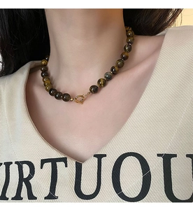 Close-up of tiger eye bead necklace with a gold metal clasp on a model’s neck