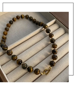 Close-up of tiger eye bead necklace with golden toggle clasp on a beige velvet surface