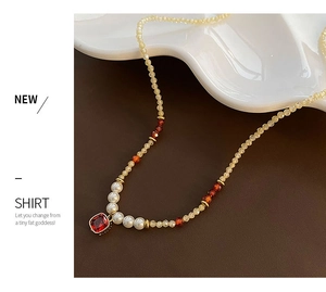 Détail du collier de perles vintage avec pendentif en pierre rouge sur plateau blanc