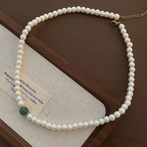 Elegant French style glass pearl necklace with a single green accent bead on a wooden tray