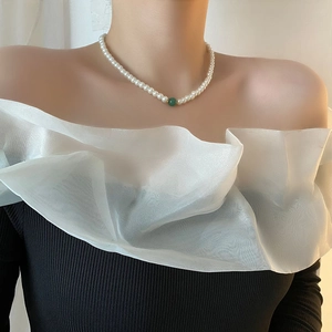 French glass pearl necklace with a central green stone pendant on a fashion model