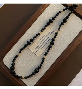 Detail of black onyx beaded necklace with gold spacers in a rustic wooden jewelry tray