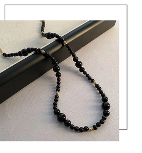 Detail of black onyx beaded necklace featuring golden hollow spheres and glossy beads