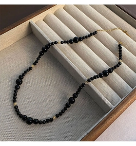 Detail of minimalist black onyx beaded necklace with gold spacers on a beige display stand